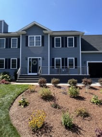 Stainless cable railing lines a gray composite front porch on a blue colonial home with fresh landscaping.