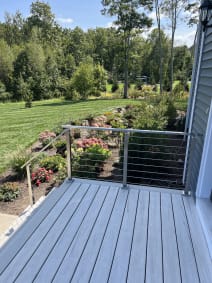 Stainless cable railing with stair rail on a gray composite deck overlooking lush flower beds and lawn.