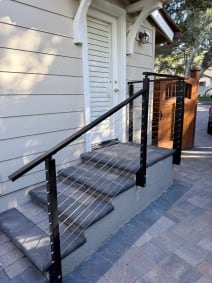 Close view of a black cable railing and handrail along slate-capped entry steps beside white siding.