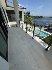 Slim side-mount rod railing runs along a stone balcony overlooking a pool and waterway.