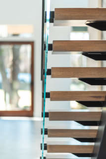 Oak floating treads with black standoff pins and glass seen in side profile against a soft background.