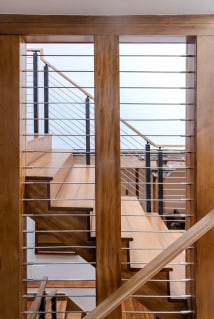 Horizontal rods with black posts and a wood handrail line a wood stair, framed through a wood doorway.