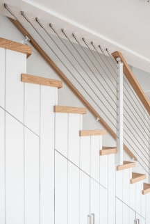Stainless cable infill and a light oak handrail along white shiplap stairs with oak treads.