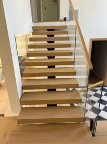 Straight white oak FLIGHT Mono stair with frameless glass on black talons and a wood handrail above a checkered floor