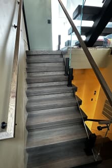 Dark-stained floating treads with frameless glass on black ascend talons and a wood handrail