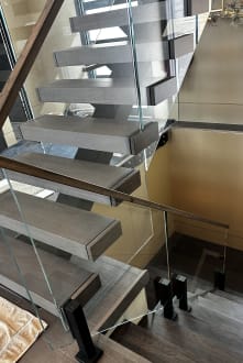Looking down dark floating treads beside frameless glass on black talons