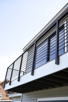 Black side-mounted posts with horizontal rod infill along a white-fascia second-story balcony.