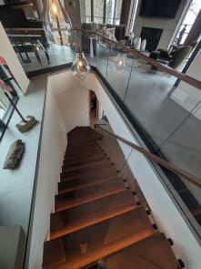 Walnut floating treads with LED lighting below a standoff-pin glass railing and walnut cap