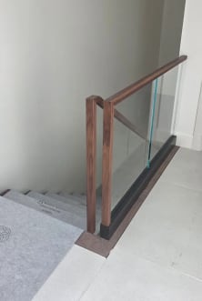 Frameless base rail glass with a walnut cap and squared walnut newel at the head of a stair