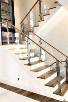 Brushed stainless posts with glass infill and an oak handrail follow a white-riser oak-tread switchback stair.