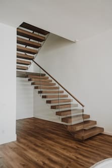 Warm wood cantilever treads float off a white wall with frameless glass and wood handrail above wood flooring.