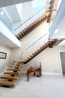 Looking up a wood mono-stringer floating stair with glass railing and a glass-railed loft above.