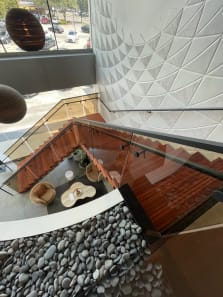 Red wood floating treads with glass railing switch back above a lounge and river-stone feature.