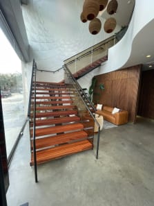 Red wood floating treads with glass railing climb beside floor-to-ceiling windows under a sculpted white ceiling.