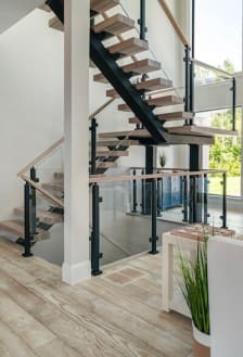 Light oak treads on a black mono stringer switchback with post-to-post glass railing and wood handrail.