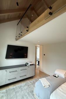 A frameless glass loft guard on black standoffs with slim black cap rises over a bedroom with oak ceiling.
