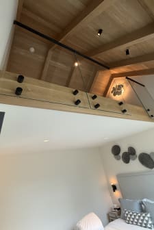 Black standoff pins secure glass panels along an oak fascia beneath warm wood ceiling beams.