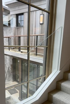 A frameless glass guard fills a tall grid window niche beside a carpeted stair.