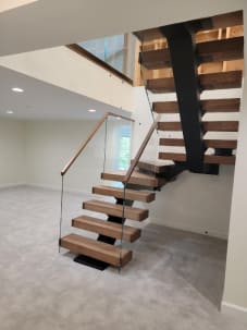 Thick wood treads on a black mono stringer rising through winders beside frameless glass with a wood handrail.