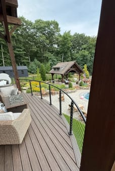 Black cable railing sweeps along a curved composite deck above a landscaped pool yard.
