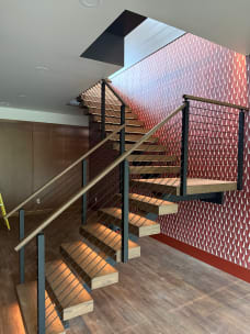 Black FLIGHT stair with white oak treads and under-tread LED lighting turns at a landing beside a red patterned wall, with cable railing.