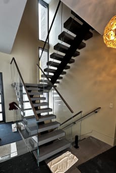 Dark floating switchback stair on a black mono stringer with frameless glass and a wood handrail
