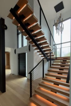 Glowing LED white oak treads and black horizontal rod railing in a tall window-lit entry