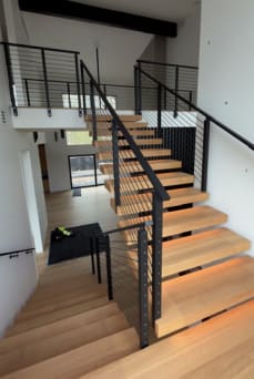 White oak switchback floating stair with LED treads and black rod railing up to a loft