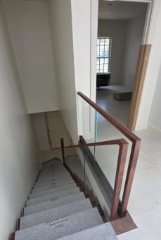 Frameless base rail glass with a walnut cap and squared walnut newel at the head of a stair