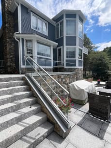Glass base rail railing with a glass-mounted handrail runs up granite steps beside a stone-walled patio
