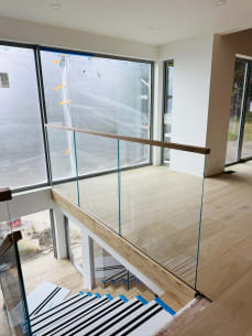 Frameless glass with a wood cap rail surrounds a stair opening beside floor-to-ceiling windows