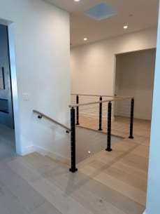 Black cable railing with white oak cap guards a stair opening on pale oak floors