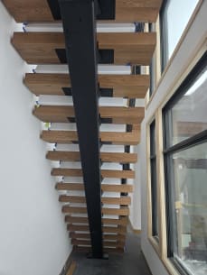 Black mono stringer with thick oak treads seen from below beside tall windows