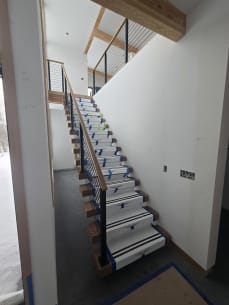 Long floating stair with black rod railing and oak handrail climbing to a loft, treads in Viewrail covers