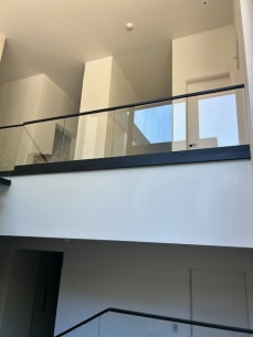 Frameless glass on a black base rail with a slim black top cap along an upper loft