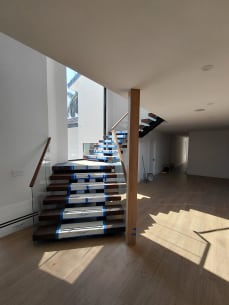 Dark floating stair with frameless glass and wood handrail beside a timber column, treads in Viewrail covers