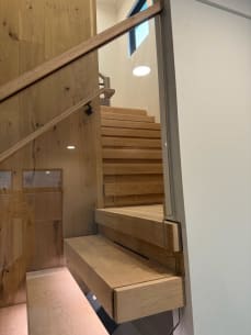 Rustic white oak floating treads and frameless glass beside a plank-clad wall