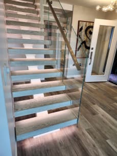 Weathered oak floating treads glowing with LED light beside frameless glass and a stainless handrail