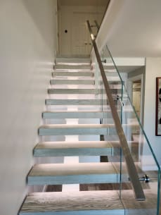 Straight run of gray-oak floating treads with LED lighting, frameless glass and a square stainless handrail