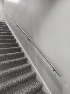 Round stainless wall handrail running up a carpeted commercial stair
