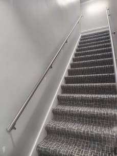 Round stainless wall handrail running up a carpeted commercial stair