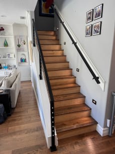 Looking up a stained wood stair with a black wall-mounted handrail and black cable railing.