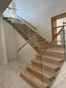 White oak stack stair with glass on brass standoff pins and a brass handrail in a bright stairwell.