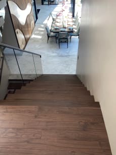 Walnut thick-nose landing and treads with frameless glass leading down to a marble-floored dining room.