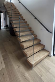 Connected oak Stack stair with frameless glass and a black wall handrail in a bright stairwell