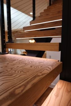 Close view of thick ash floating treads with LED lighting and black cable railing