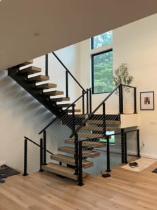Light oak treads on black mono stringers turning at a landing with black post cable railing.