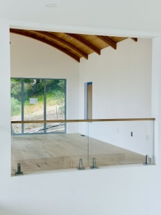 Frameless glass on talon spigots with a wood cap rail overlooks a bright room with a curved wood ceiling