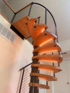 Wood spiral treads with glowing LED edges wind up a black center column to a cable-railed landing.