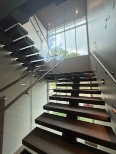 Dark wood FLIGHT Mono treads with Vedera glass and stainless handrails rise toward a two-story window.
